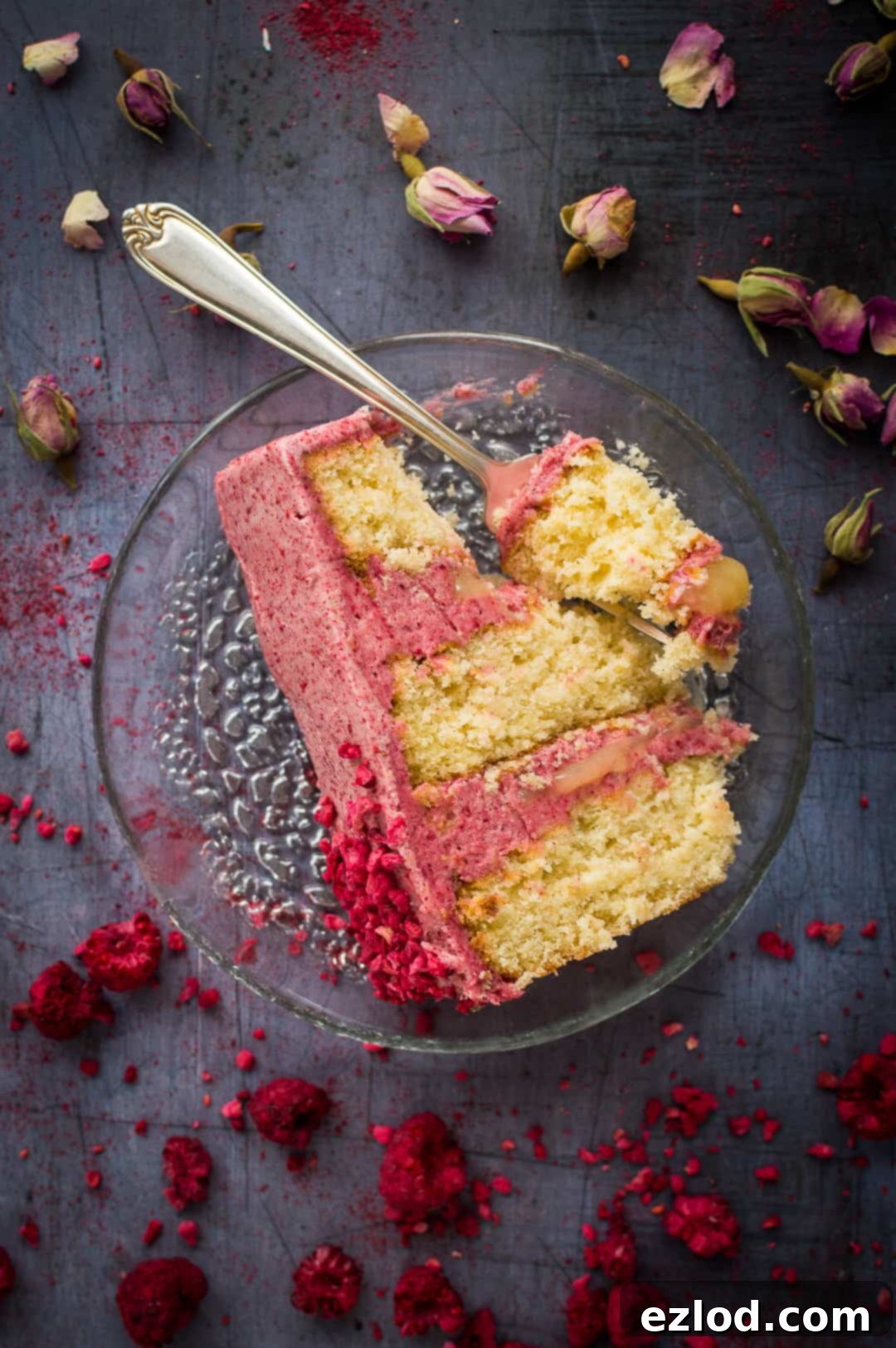 A perfectly cut slice of three-layered coconut cake, revealing fluffy pink raspberry cooked flour frosting and bright yellow lemon curd filling, presented on a white plate.