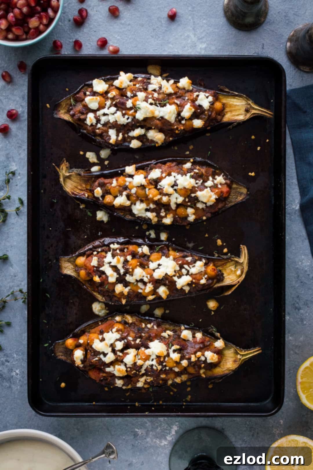Roasted aubergines stuffed with chickpeas and lentils toppedwith feta on a black baking tray.
