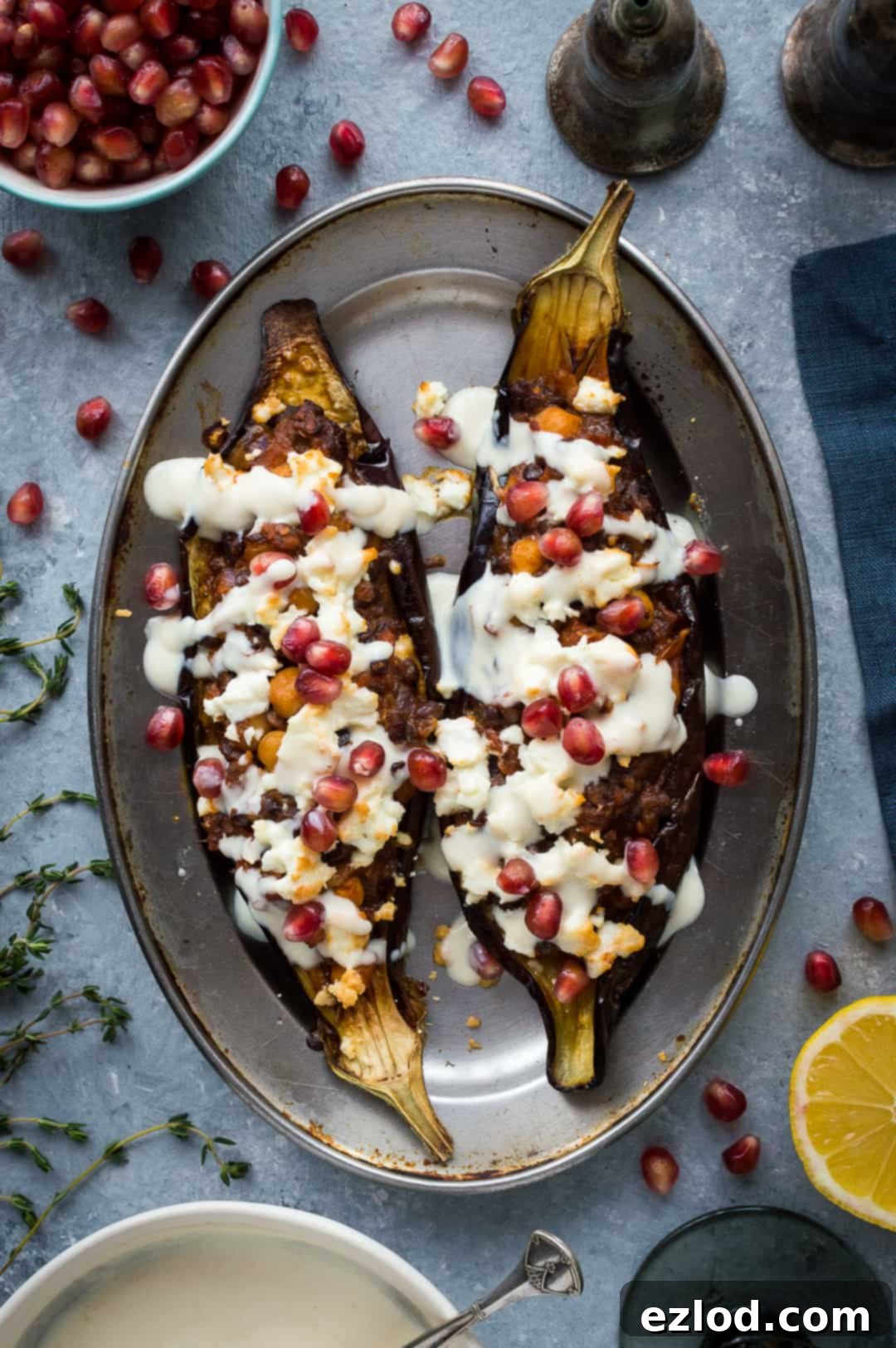 Top down photo of two stuffed eggplants with lemon tahini yogurt sauce and pomegranate.