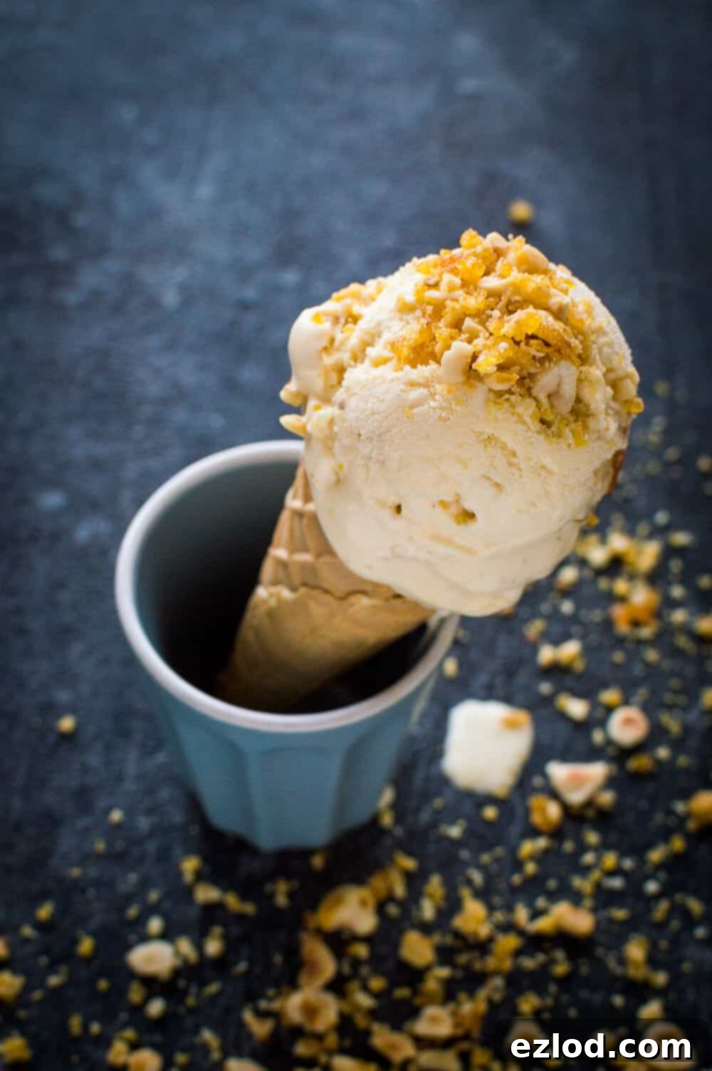 A scoop of hazelnut praline ice cream in a waffle cone sprinkled with crushed hazelnut praline.