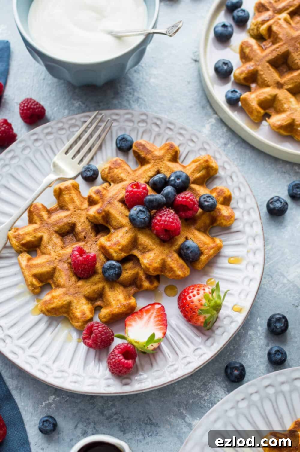 A beautifully presented plate featuring healthier sweet potato waffles, adorned with a colorful medley of fresh berries and a generous drizzle of golden maple syrup.