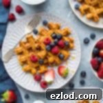 A vibrant close-up of golden-brown sweet potato waffles, artfully topped with a colorful medley of fresh berries and a generous cascade of maple syrup, signaling a delightful breakfast experience.