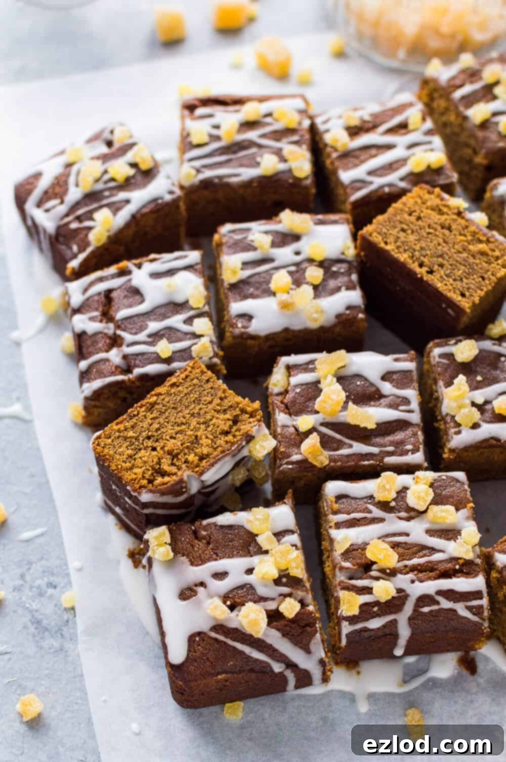 Perfectly cut squares of vegan ginger traybake cake, adorned with a delicate lemon glaze and a sprinkle of candied ginger, arranged on a subtle light grey backdrop.