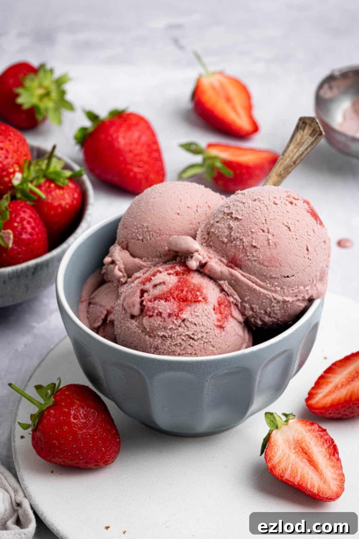 Vegan strawberry ice cream in a grey bowl with a bowl of fresh strawberries.