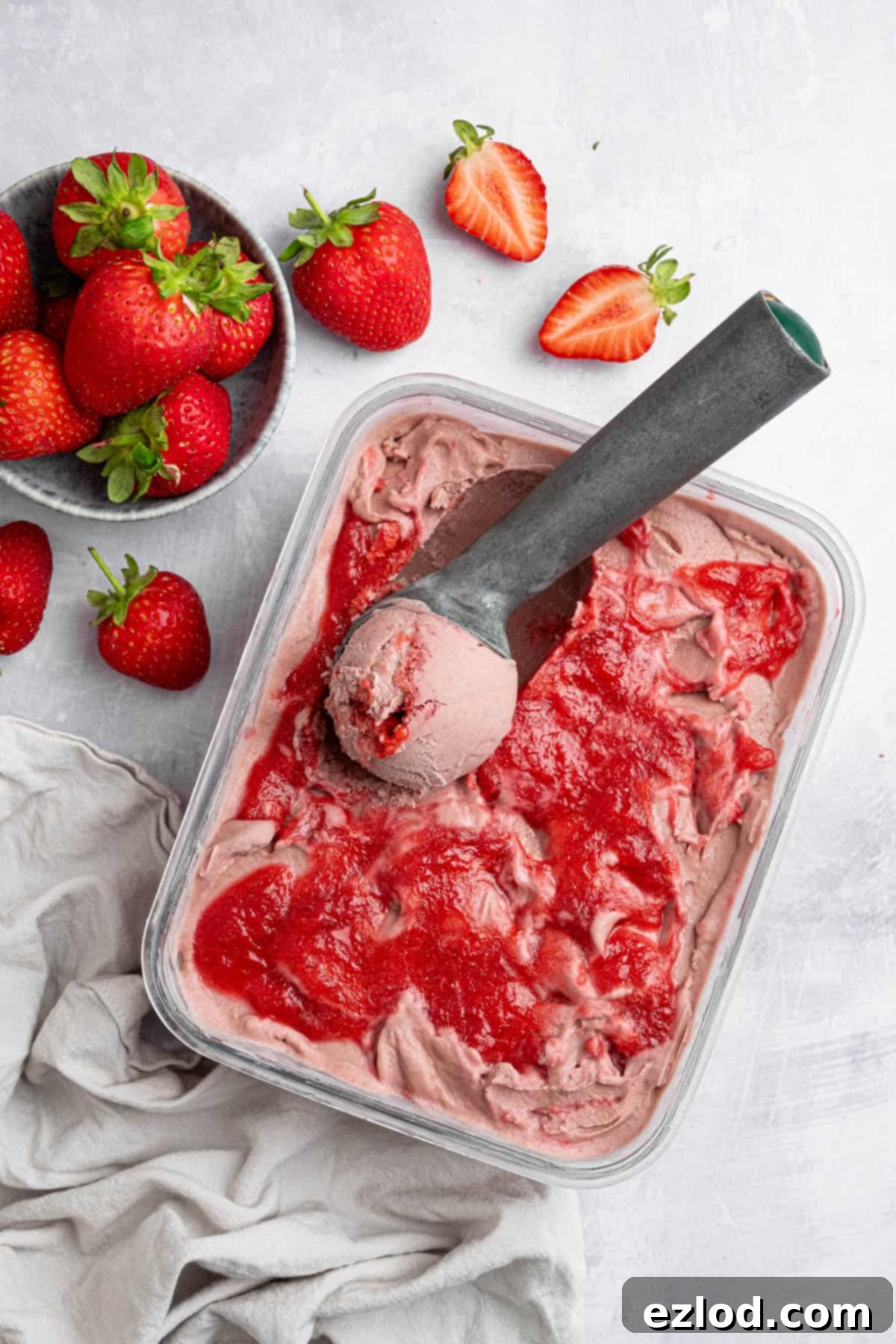Vegan strawberry ice cream in a glass container with an ice cream scoop.