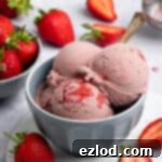Vegan strawberry ice cream in a grey bowl with a bowl of fresh strawberries.
