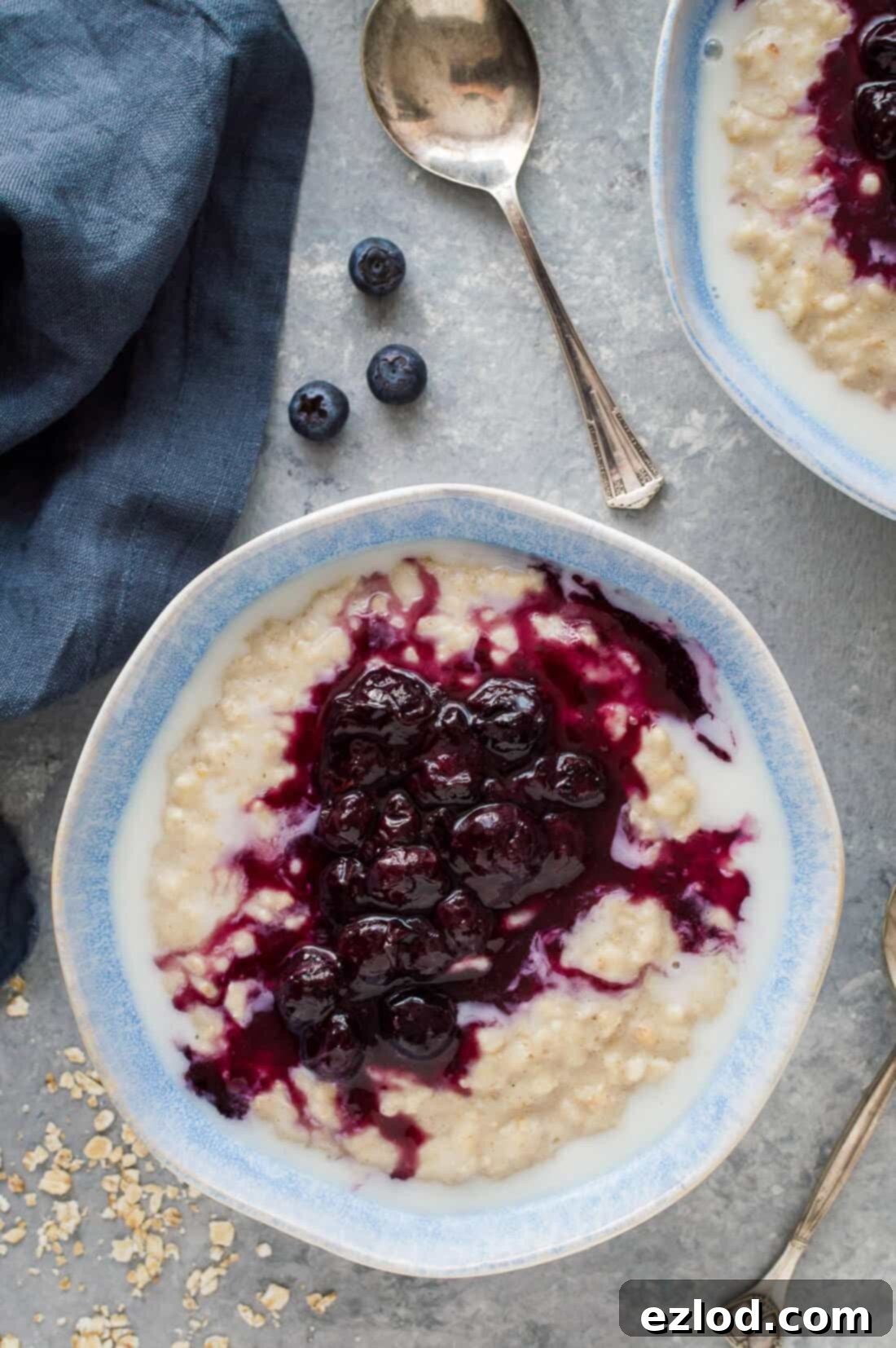 Golden Banana Oats with Blueberry Swirl 4 Two bowls of creamy banana porridge topped with vibrant blueberry compote, arranged on a grey background, showcasing a delightful and healthy breakfast.