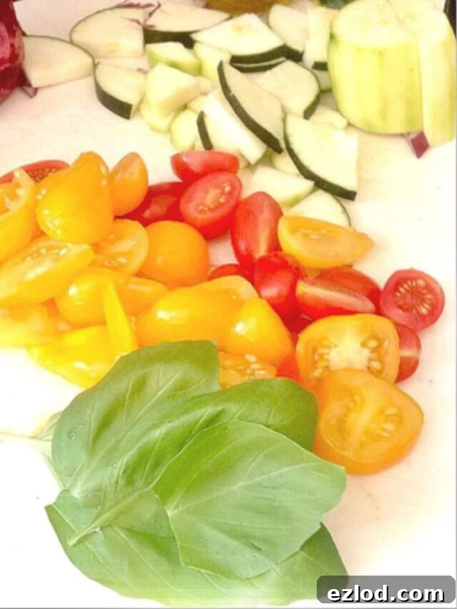 Fresh basil, halved tomatoes, and sliced zucchini are displayed on a cutting board