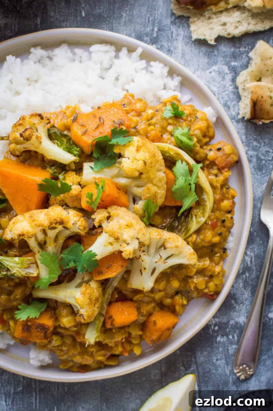 A close-up shot of a plate featuring a generous serving of vegan red lentil dhal with fluffy white rice, adorned with perfectly roasted cauliflower and tender butternut squash.