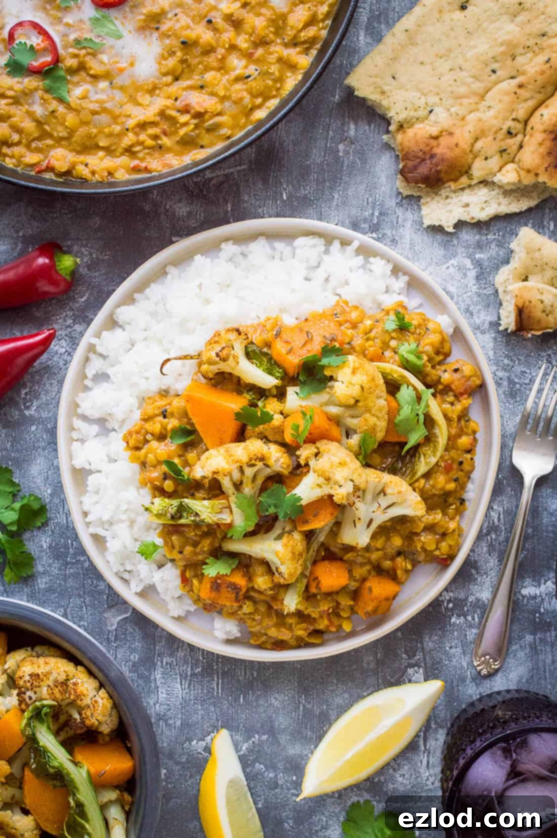 A plate of red lentil dhal, served alongside fluffy white rice, and topped with golden roasted cauliflower and butternut squash, ready to be enjoyed.