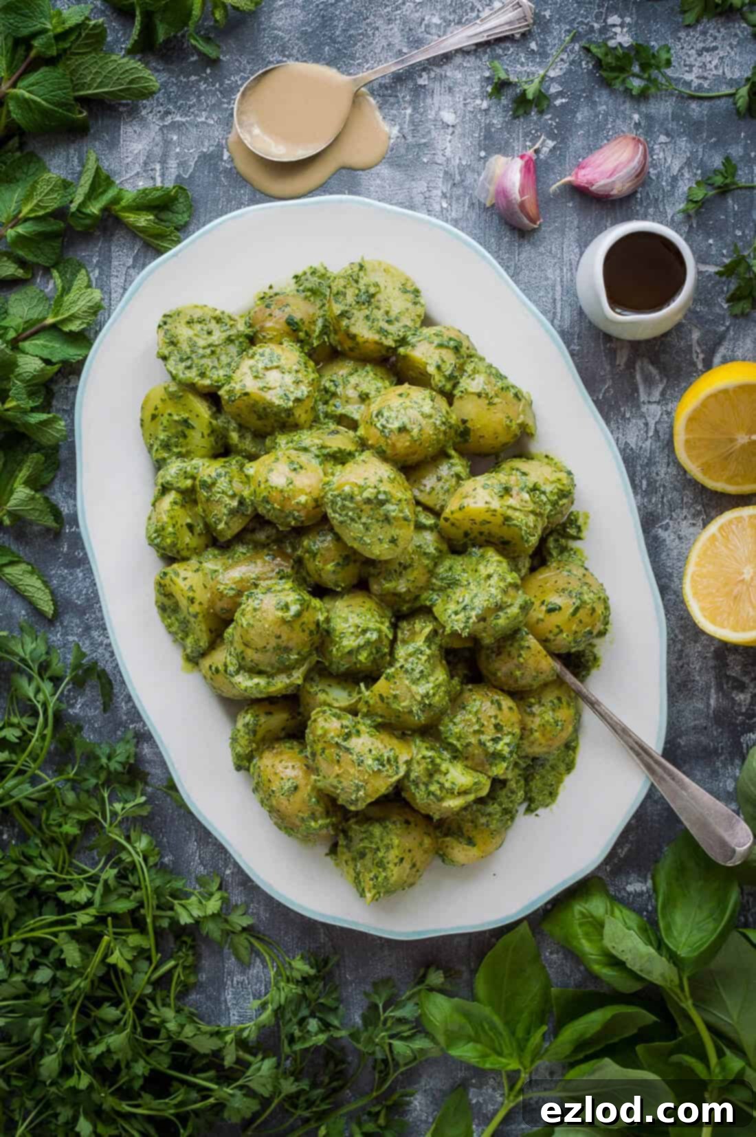A platter of potato salad with tahini herb dressing surrounded by herbs.