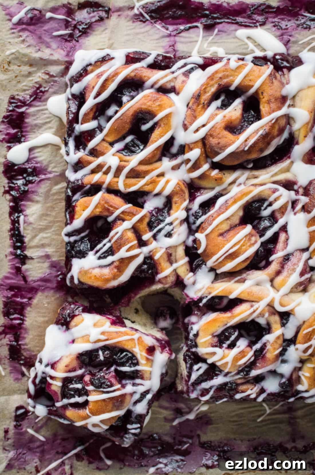 A top down shot of vegan lemon blueberry sweet rolls drizzled with lemon glaze on a sheet of baking parchment