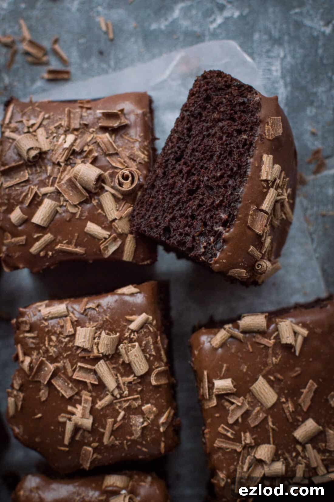Photo of a square of vegan chocolate sheet cake with coconut milk ganache and chocolate curls on it's side.
