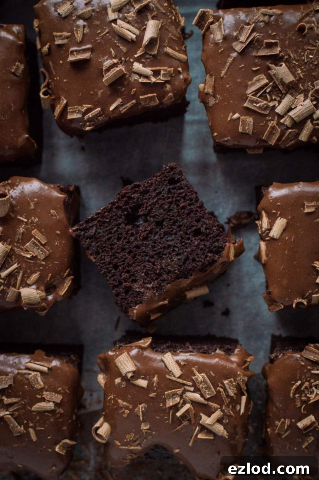 Squares of vegan chocolate traybake cake with vegan ganache, one slice on it's side.