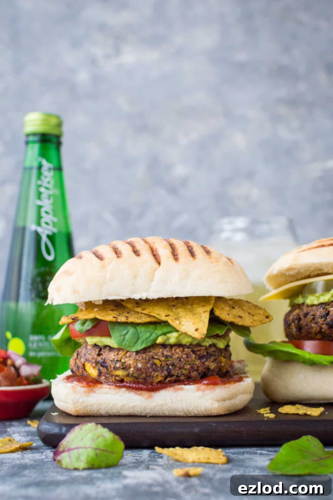 Close-up of a vegan Mexican bean burger with creamy guacamole, crispy tortilla chips, and a refreshing Appletiser beverage.