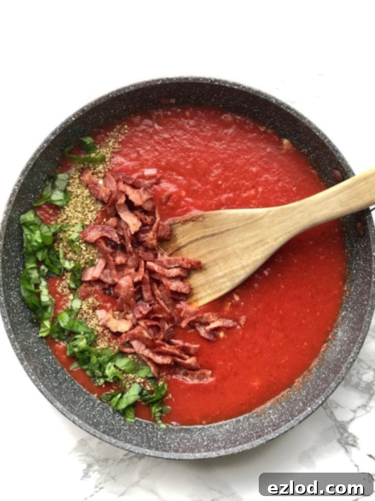A overhead shot of a skillet with red sauce, basil, oregano, and turkey bacon. 