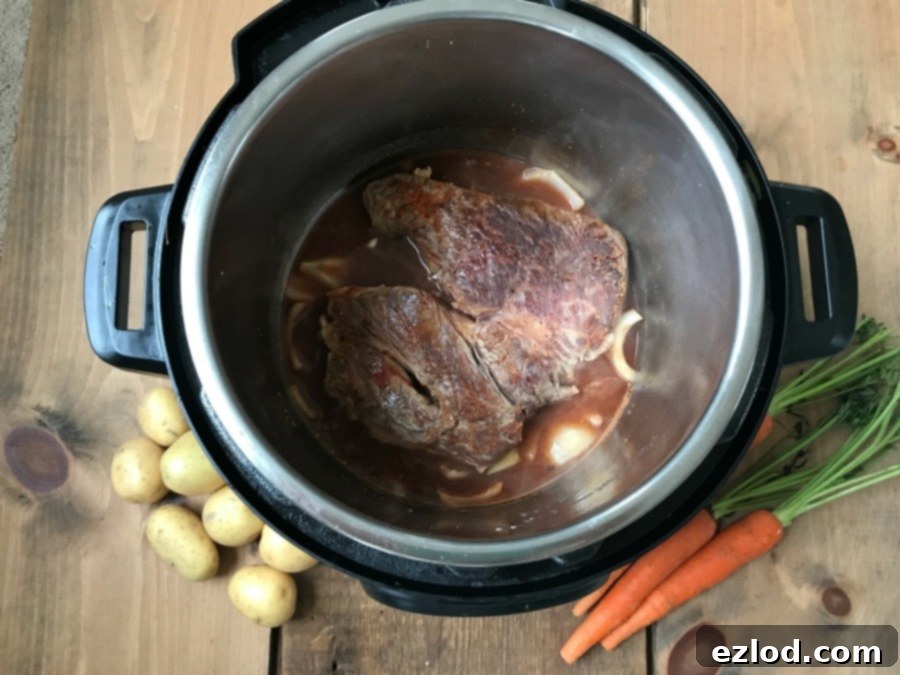A photo of an open Instant Pot with a roast at the bottom next to some carrots and potatoes
