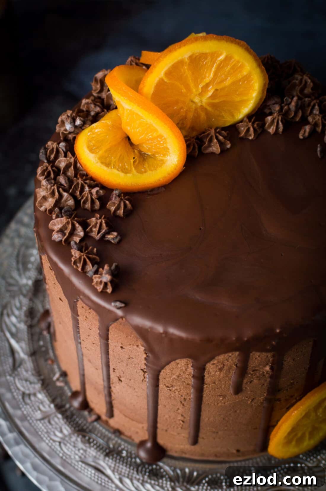Close up of vegan orange and almond cake with chocolate buttercream, chocolate drip, candied oranges and cacao nibs.