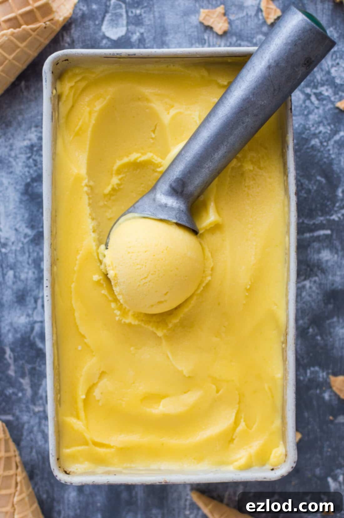 A tub of vegan mango lassi sorbet with an ice cream scoop.
