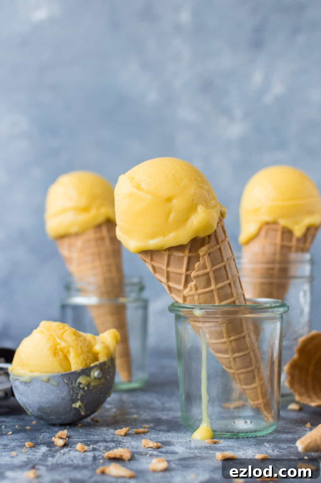 Scoops of vegan mango lassi sorbet in waffle cones on a grey background.