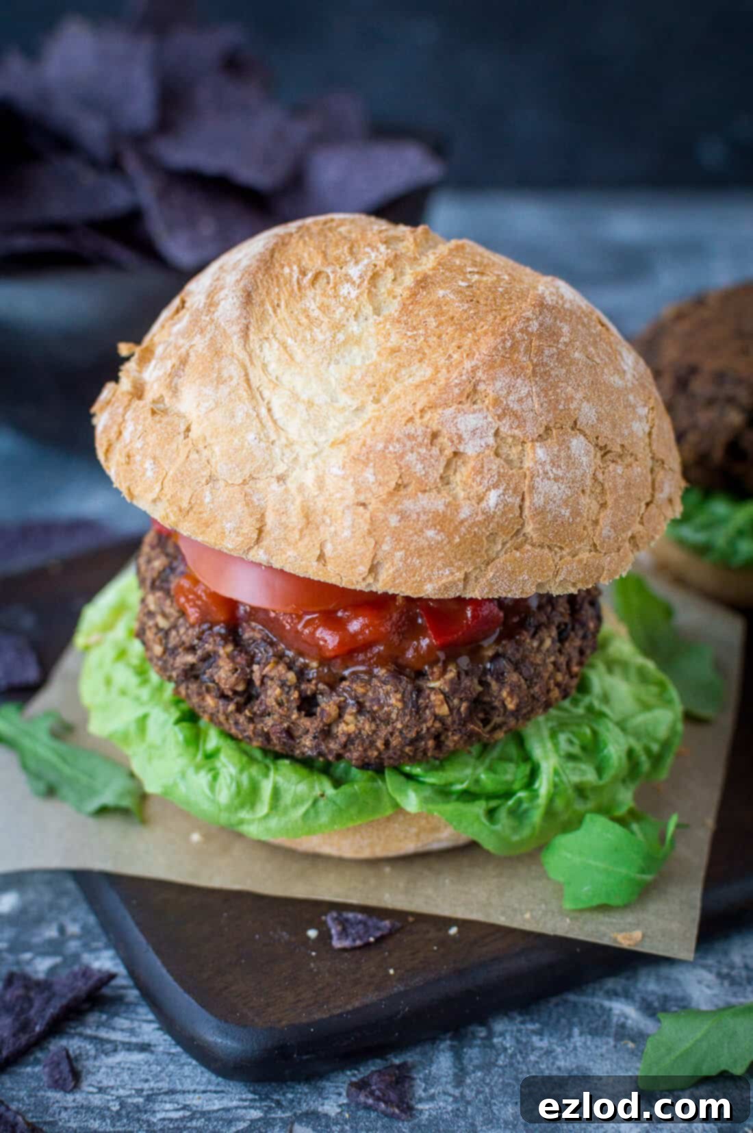 A close-up of a perfectly constructed vegan mushroom, lentil, and walnut burger nestled in a soft roll with crisp lettuce and a vibrant tomato salsa, showcasing its hearty texture.