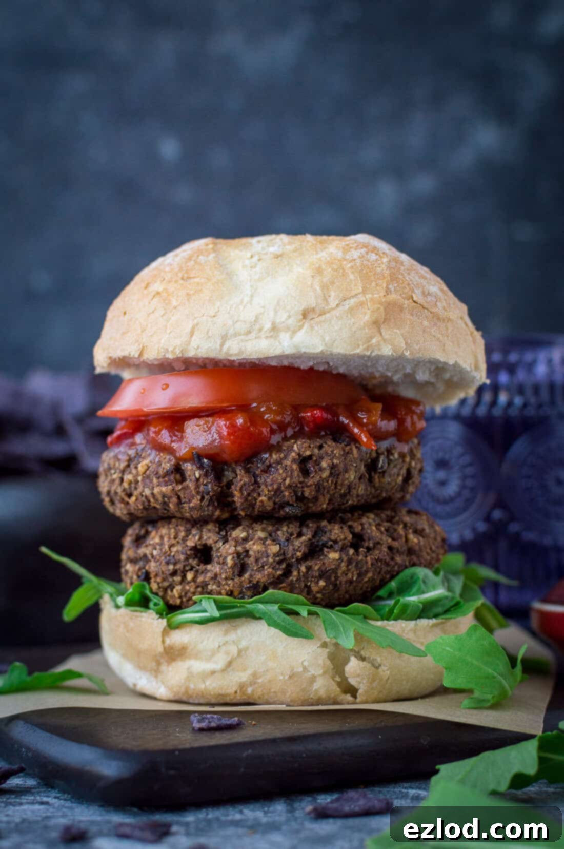 Two hearty vegan mushroom lentil walnut burgers stacked in a soft bun, garnished with fresh lettuce and tomato, presenting a tempting and substantial plant-based meal.