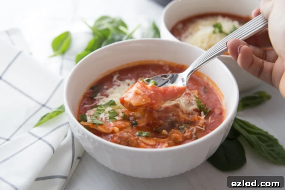 A bowl of Instant Pot Lasagna Soup sitting next to a blue and white kitchen towel. Fresh basil leaves are scattered around the table