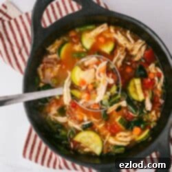 Set-It-and-Forget-It Chicken Vegetable Soup 2 A cast iron pot of Chicken Vegetable Soup on a red and white striped kitchen towel with a small bowl of parmesan cheese off to the side.