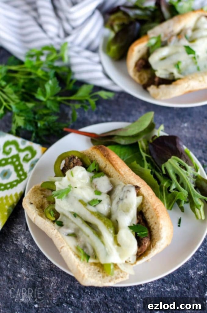 Philly cheesesteak sandwich topped with peppers, onions, and provolone cheese with a side salad on a white plate and blue background