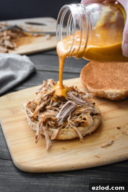Pulled pork made in the instant pot, on half of a bun, drizzled with BBQ sauce pouring from a glass mason jar