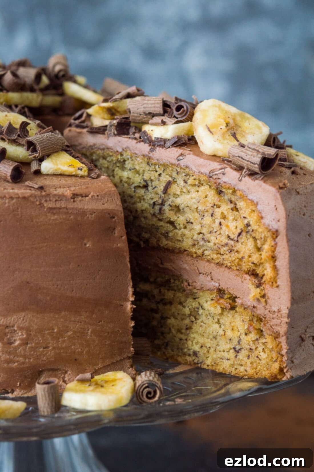 Close up of sliced vegan banana cake with chocolate peanut butter buttercream, banana chips and chocolate curls.