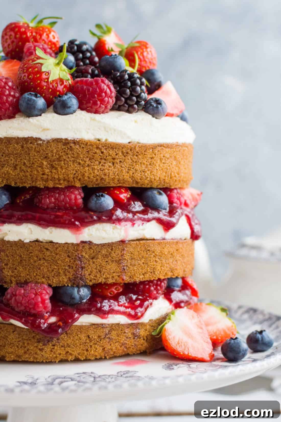 A side shotof vegan vanilla cake filled with vanilla buttercream, raspberry jam and berries on a grey background.
