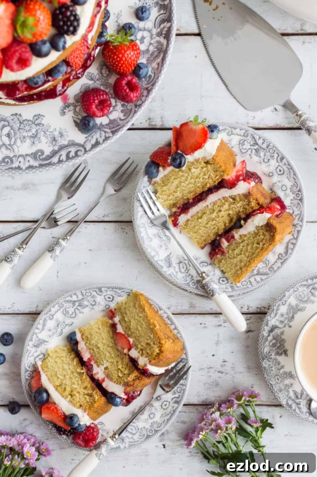 Slices of vegan vanilla cake with vanilla buttercream, berries and jam on grey plates on a white wooden background.