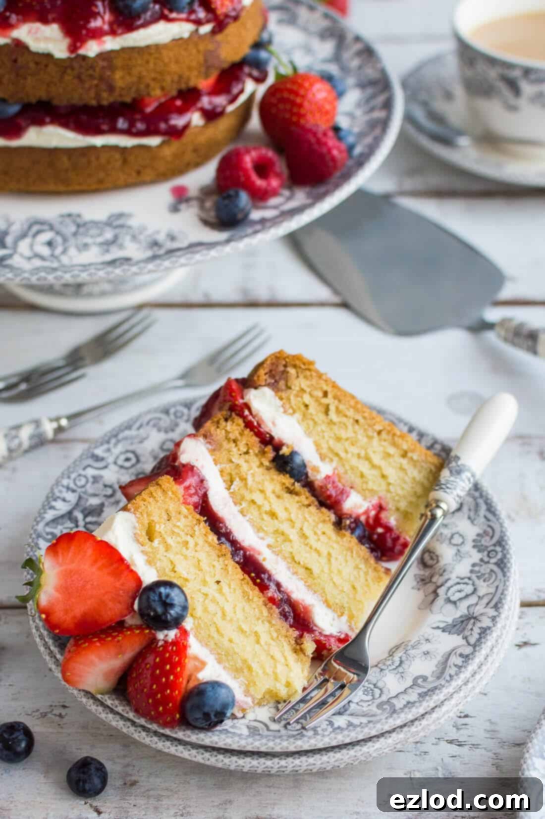 A slice of vegan vanilla cake with berries and jam on a grey Spode Delamere Rural plate with pastry fork.