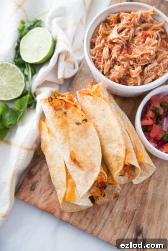 Crispy Air Fryer Chicken Taquitos, freshly cooked and served alongside a bowl of shredded salsa lime chicken, fresh salsa, and lime wedges, highlighting the delicious filling.