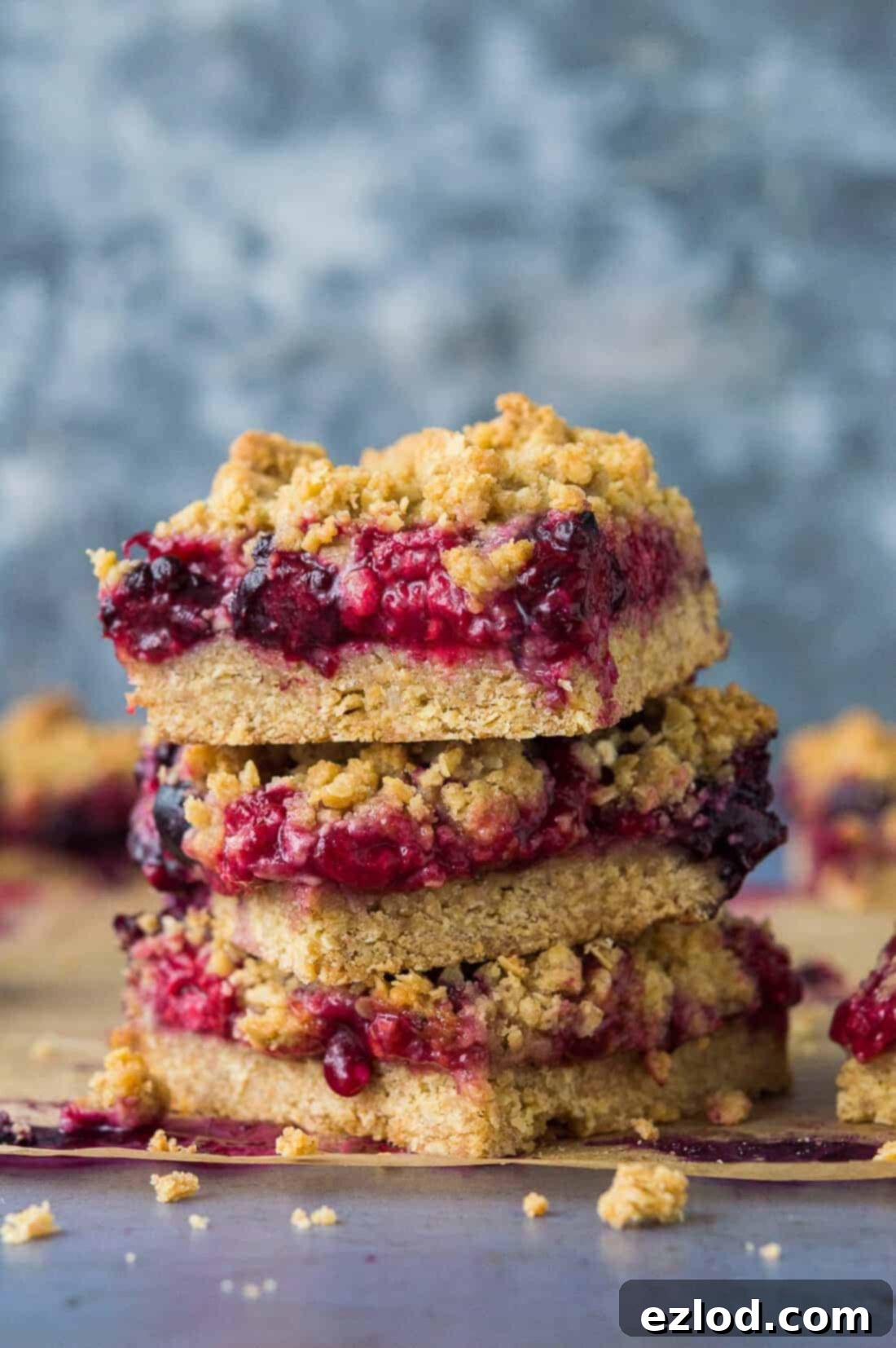 A stack of three vegan berry crumble bars, showcasing their golden crumb topping and vibrant berry filling.