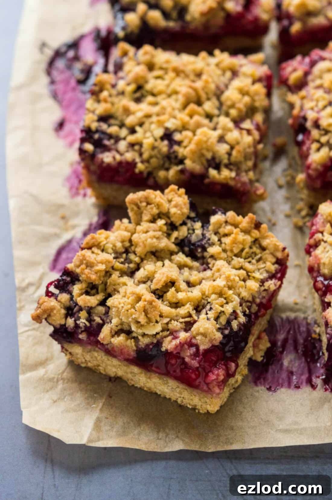 Angled shot of vegan berry oat crumble bars resting on baking parchment, showing their golden-brown edges.