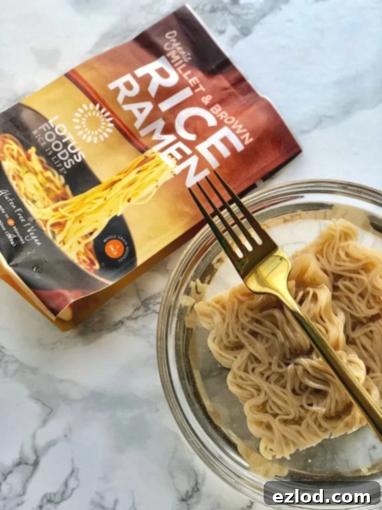 A close-up of Lotus Foods Millet and Brown Rice Ramen noodle cakes softening in a bowl of hot water on a sleek marble surface, ready for stir-frying. 