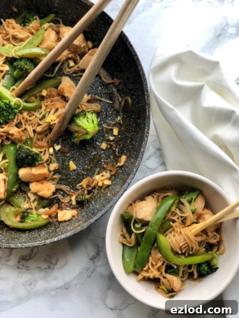A small white bowl containing a perfectly portioned serving of 21 Day Fix Chicken and Ramen Noodle Stir Fry, artfully arranged next to the generous skillet it was served from.