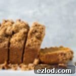 A side shot of sliced vegan sweet potato loaf cake with pecan streusel topping on a marble board and grey background.