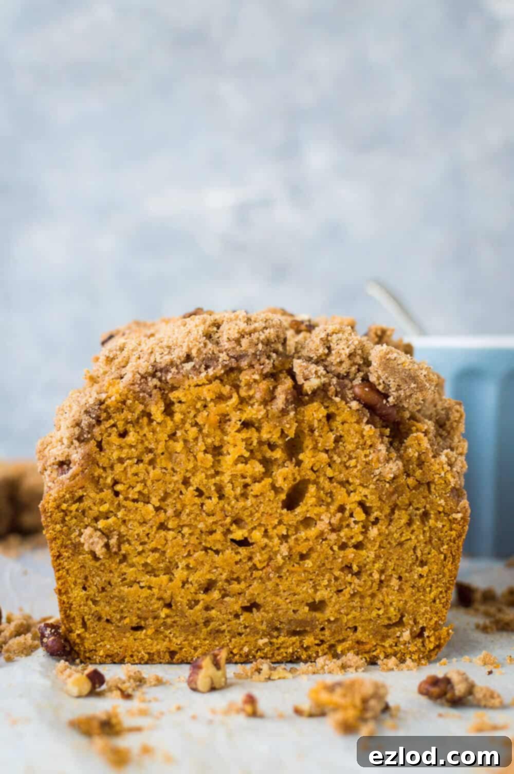 A face-on close-up photo of a whole vegan sweet potato loaf topped with pecan crumble, positioned on a chic grey background.