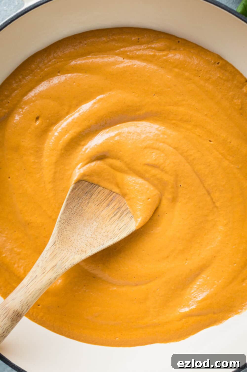 Close up of a pan of vegan creamy roasted red pepper tomato pasta sauce with a wooden spoon.