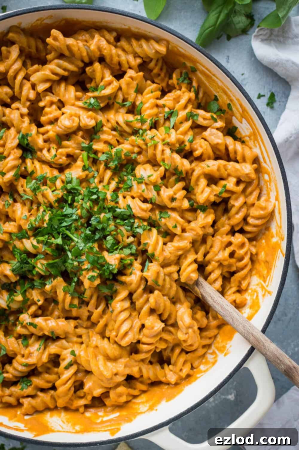 Close up of a pan of vegan creamy roasted red pepper tomato pasta topped with chopped herbs.