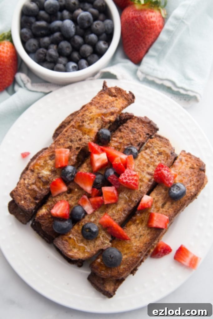 An overhead shot of a delightful plate of golden-brown Air Fryer French Toast Sticks, generously garnished with fresh mixed berries, invitingly placed on a white surface.