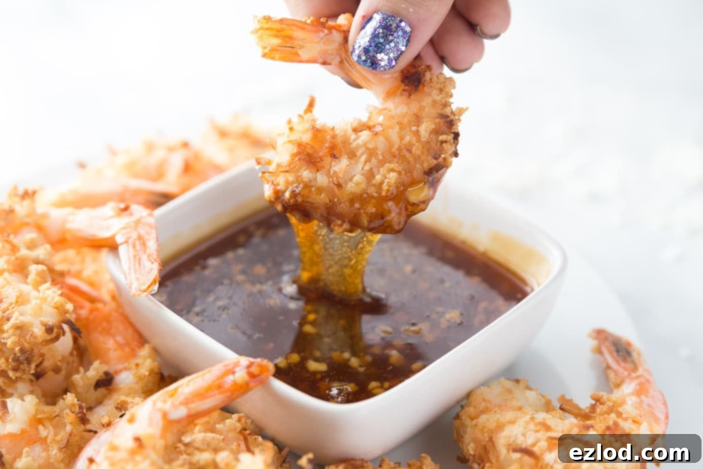 An air fried coconut shrimp is being dipped into some homemade thai sweet chili sauce