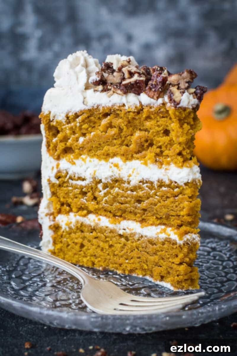 A close-up of a beautifully decorated vegan pumpkin layer cake, topped with cinnamon buttercream and maple pecans, ready to be sliced. #vegan #pumpkinspice #layercake #pumpkin #plantbaseddessert