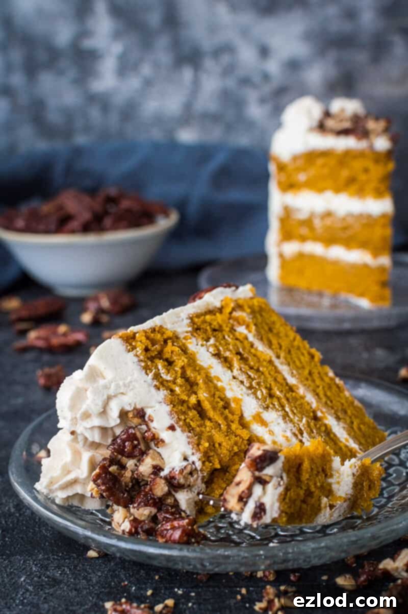 Close up of a slice of vegan pumpkin layer cake on a glass plate with a forkful taken out, showing the moist crumb and creamy cinnamon buttercream.