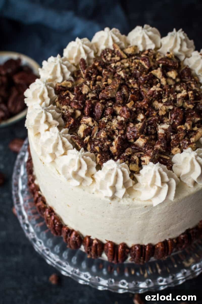 Top view of a decadent vegan pumpkin cake, generously topped with chopped maple pecans and delicate blobs of cinnamon buttercream piping.