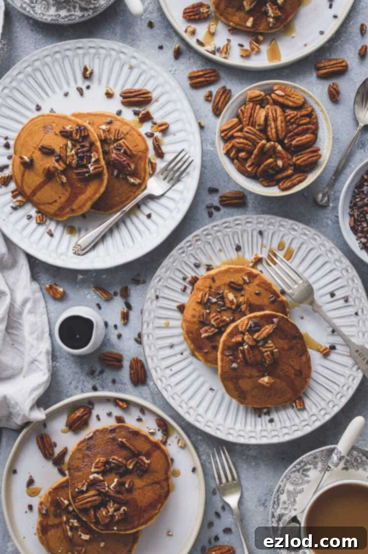 Close-up shot of a stack of fluffy vegan pumpkin pancakes with a fork resting on them, showing their light and airy texture. Drizzled with maple syrup and topped with pecans, ideal for a seasonal breakfast. #vegan #pumpkin #pumpkinspice #pancakes #brunch