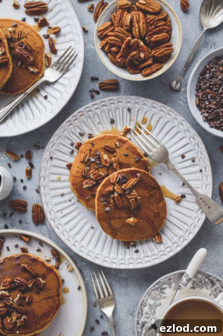 Plates of fluffy vegan pumpkin pancakes, generously topped with golden maple syrup, toasted pecans, and dark cacao nibs, arranged for a delightful autumn breakfast spread. #vegan #pumpkin #pumpkinspice #pancakes #brunch #veganbreakfast